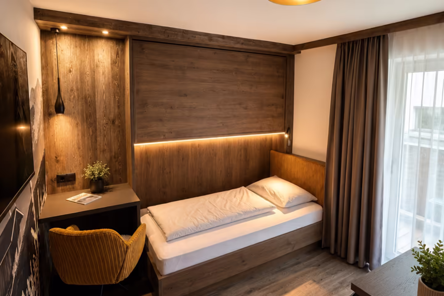 Einzelbett mit kleinem Schreibtisch und gelben Stuhl, Fenster und moderner Einrichtung